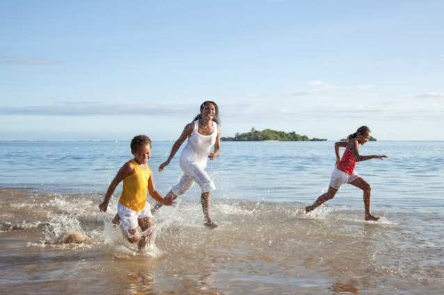 A mother and two kids run along the beach while laughing together in Fiji